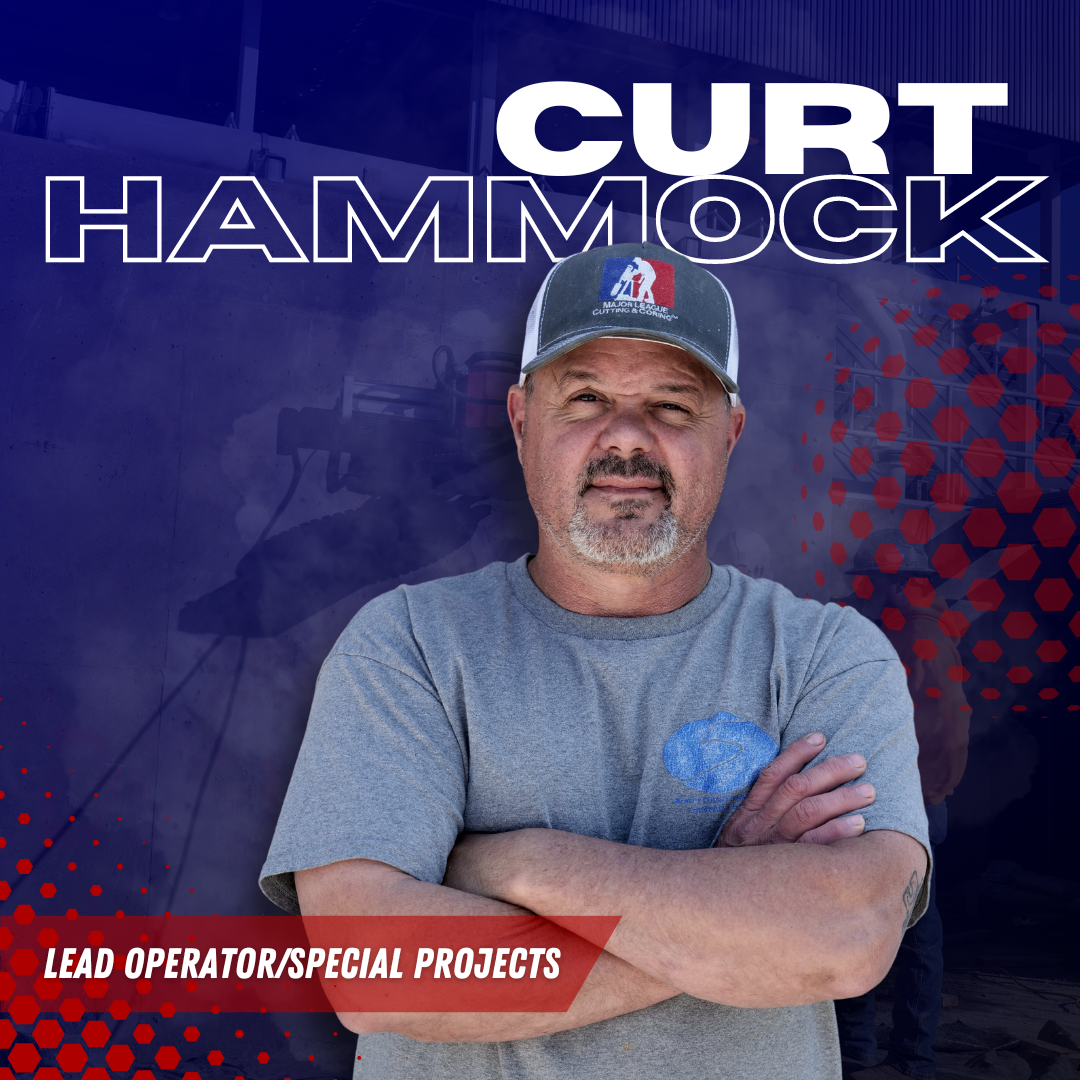 A man wearing a hat and a gray shirt is standing with his arms crossed.