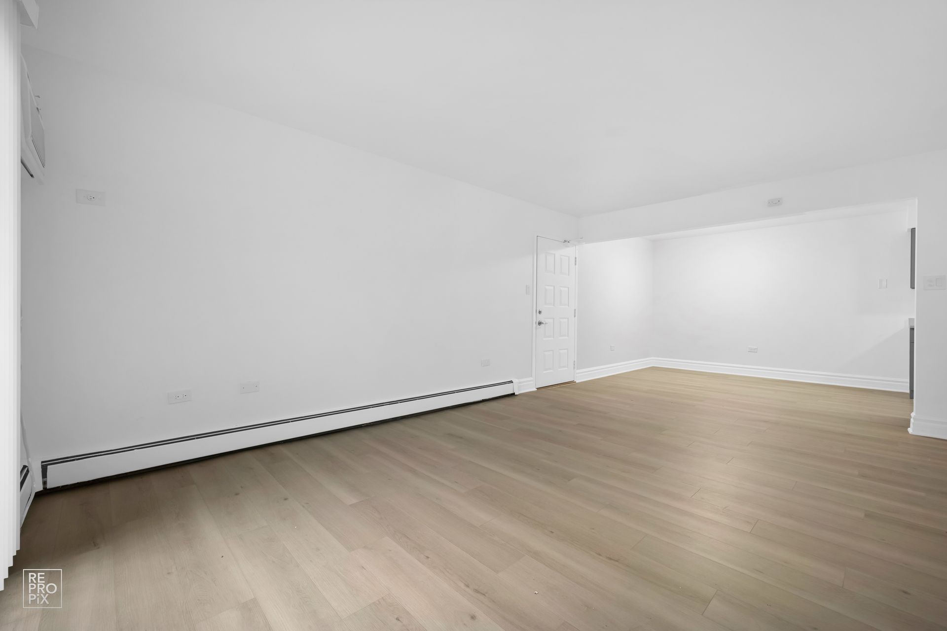 An empty living room with hardwood floors and white walls.