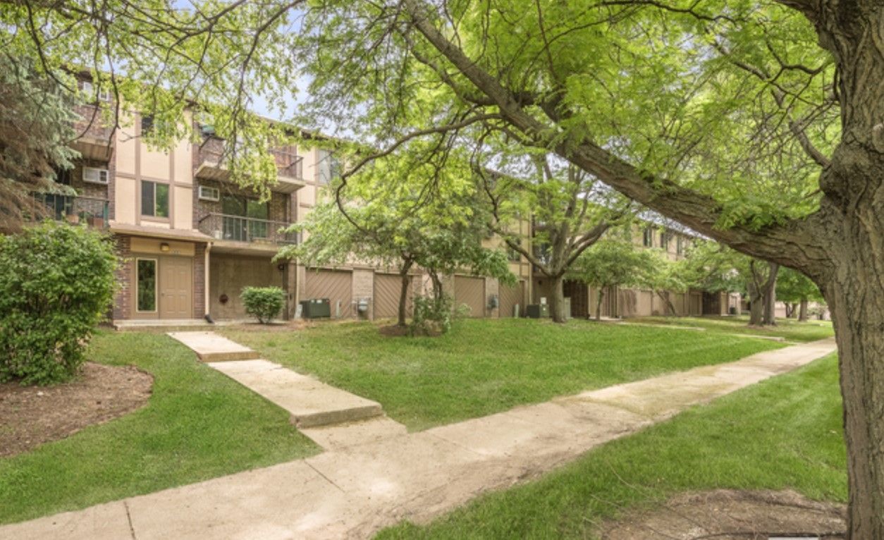 A row of apartment buildings with a sidewalk and trees in front of them.