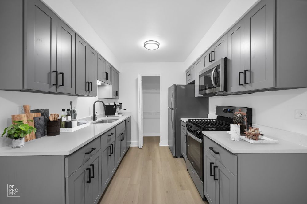 A kitchen with gray cabinets , a stove , a refrigerator , and a sink.