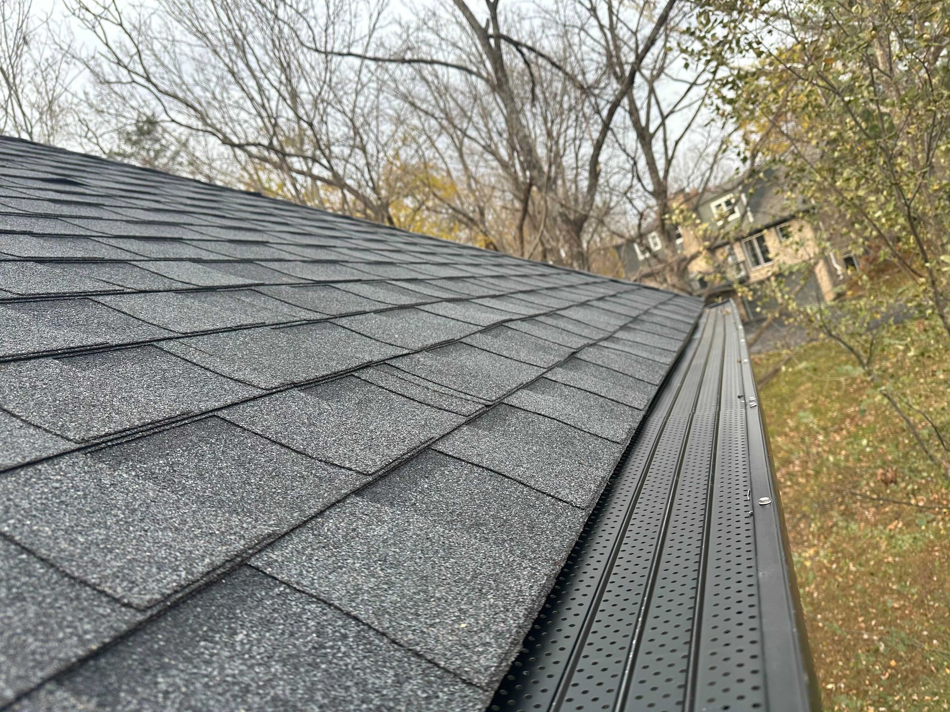 Person on roof installing gutter guard. Gray shingles, silver gutter guard, cutting tool.