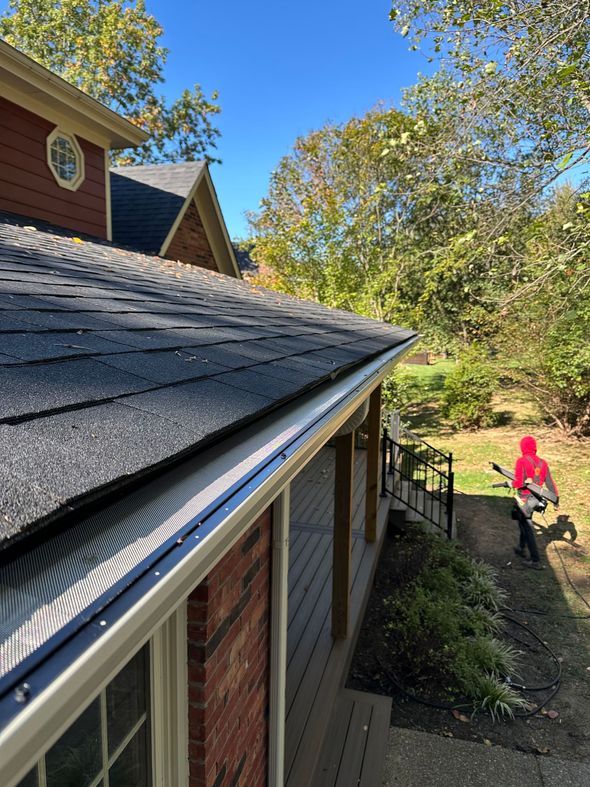 Dark gray shingle roof with black gutter guard in an outdoor setting with trees.