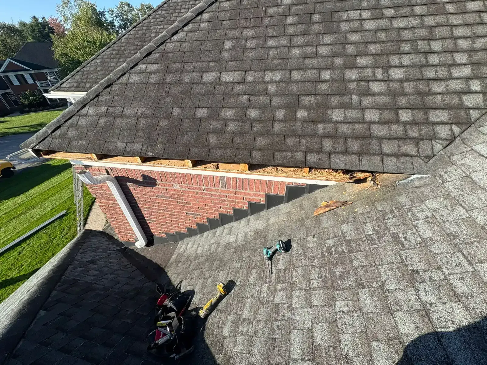 Damaged roof section exposing brick, missing shingles. Tools on roof; sunny daytime.