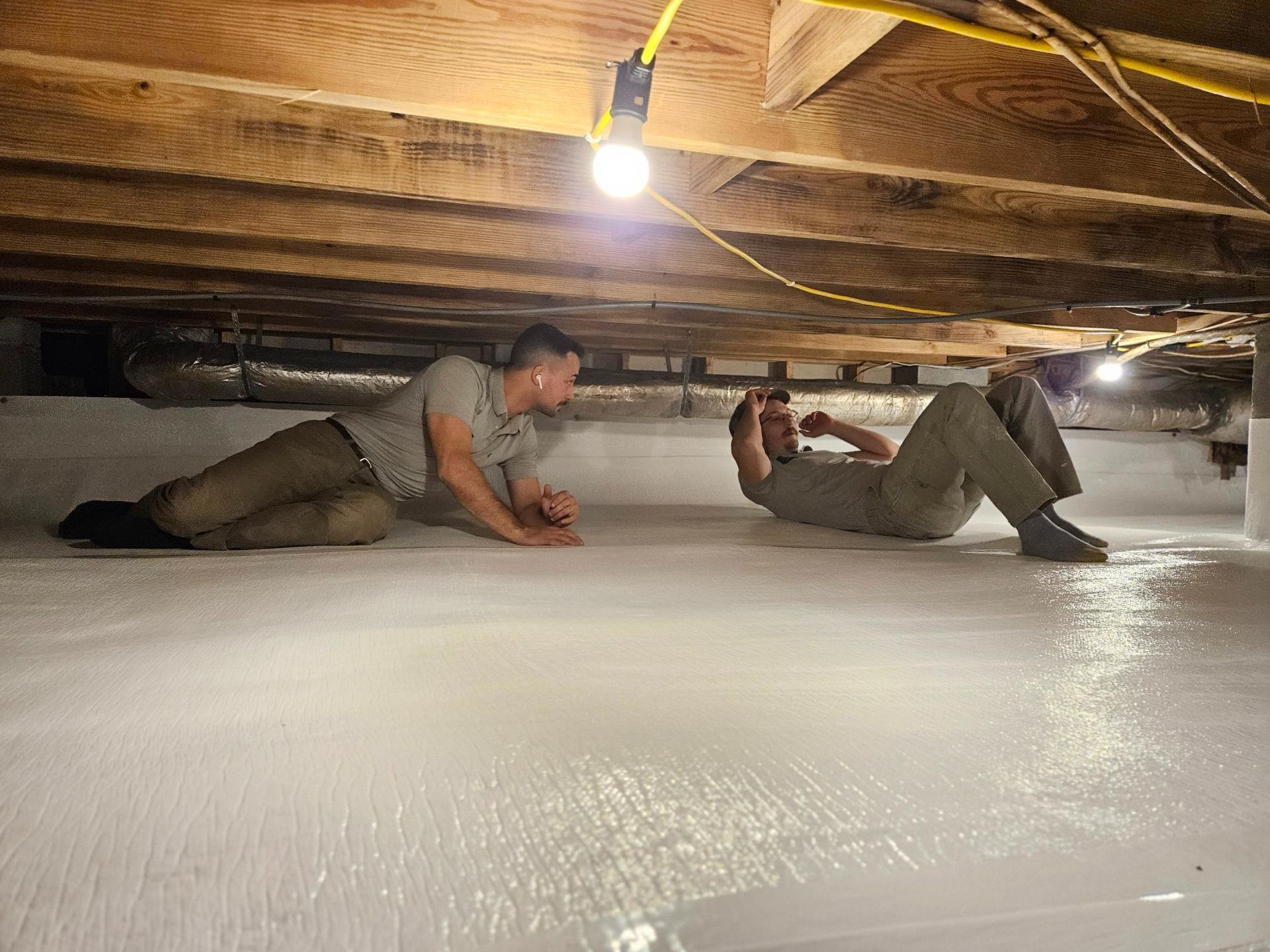 Two men are crawling under a ceiling in a basement.