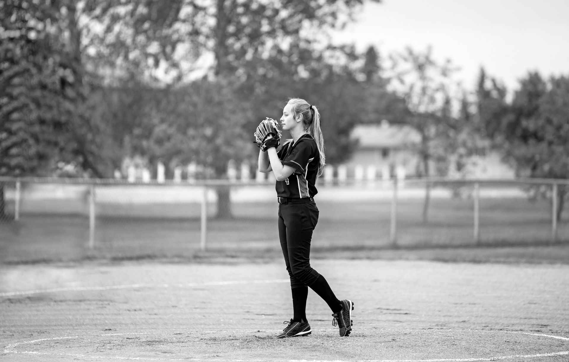 A black and white photo of a girl playing softball on a field.