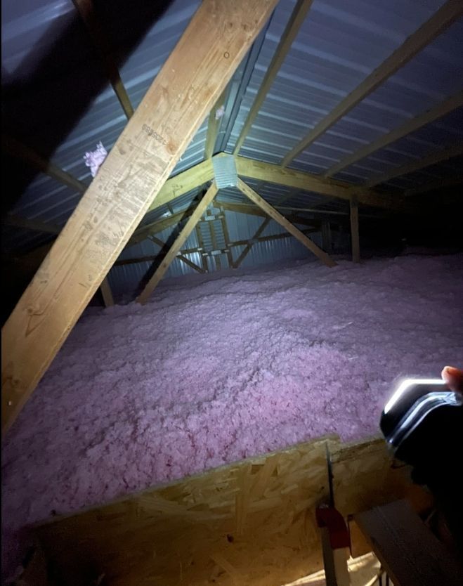A person is holding a flashlight in an attic filled with pink insulation.