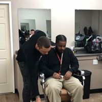 A man is sitting in a barber chair getting his hair cut by another man.