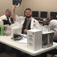 A man in a lab coat is sitting at a table holding up a piece of paper.