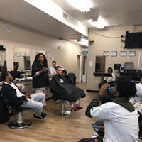 A group of people are sitting in barber chairs in a barber shop.