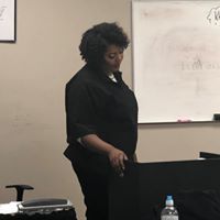 A woman is standing in front of a whiteboard in a classroom.