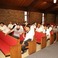 A group of people are sitting in rows of red benches in a church.