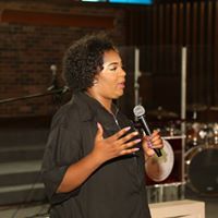 A woman is speaking into a microphone in front of a drum set.
