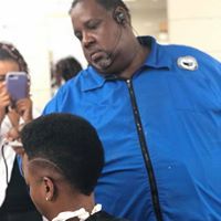 A man in a blue jacket is cutting a man 's hair in a salon.