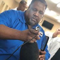 A man in a blue shirt is holding a microphone and a cell phone.