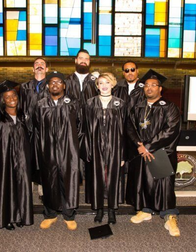 A group of graduates pose for a picture in front of a stained glass window