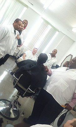 A group of men are standing around a man in a barber chair.