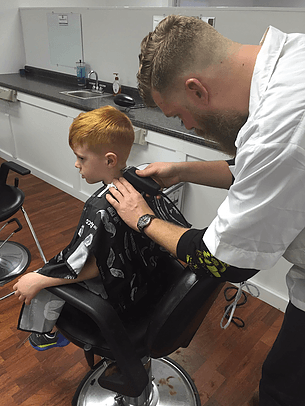 A young boy is getting his hair cut by a barber in a barber shop.