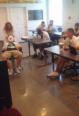 A group of people are sitting at tables in a classroom.