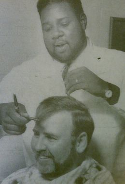 A man is getting his hair cut by a barber in a black and white photo.