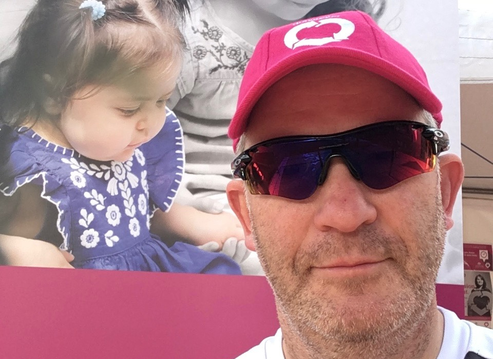 Man in pink cap and sunglasses, standing in front of a large poster featuring a child.