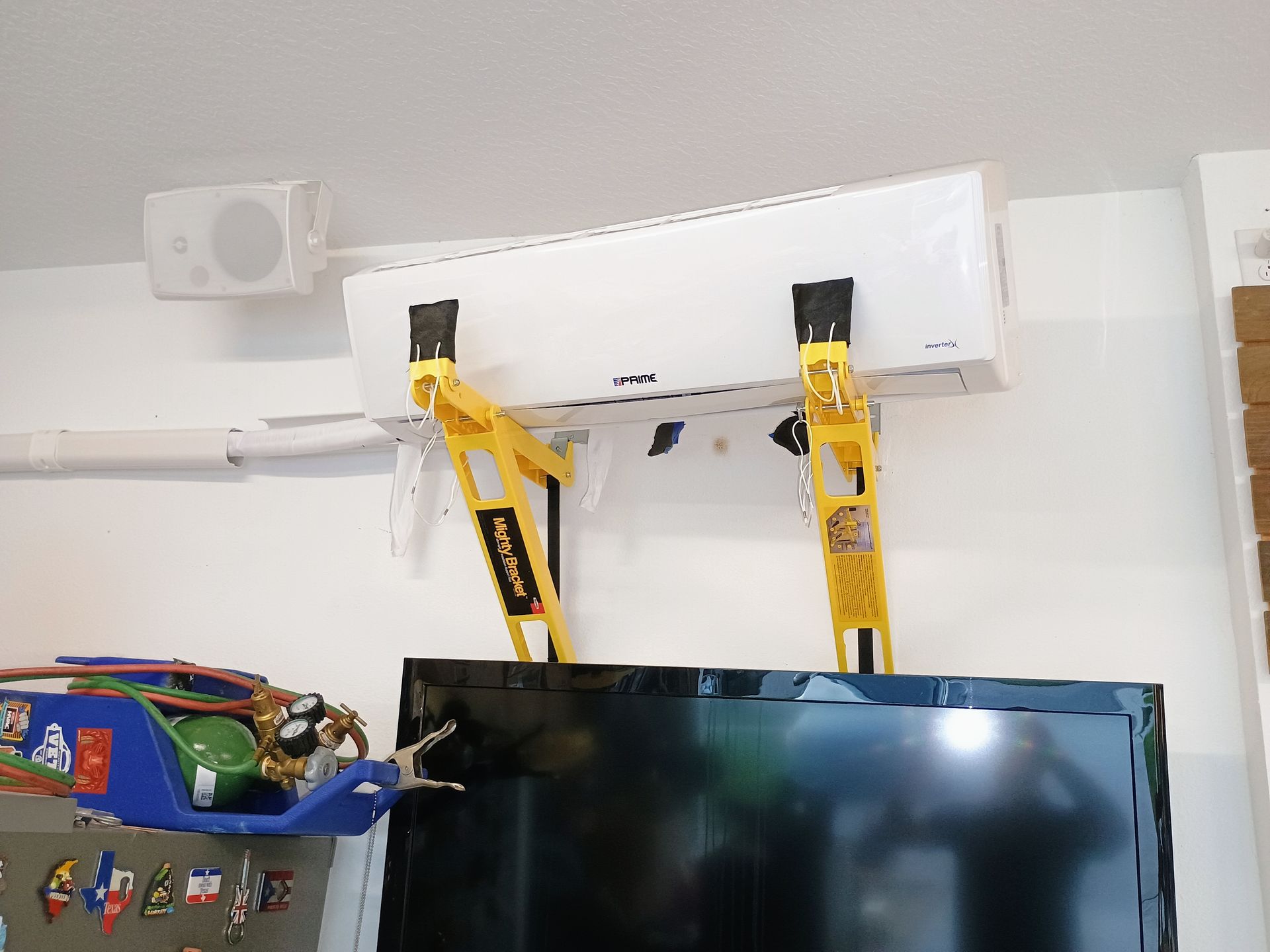 Air conditioning unit mounted above a TV, supported by yellow bracing.