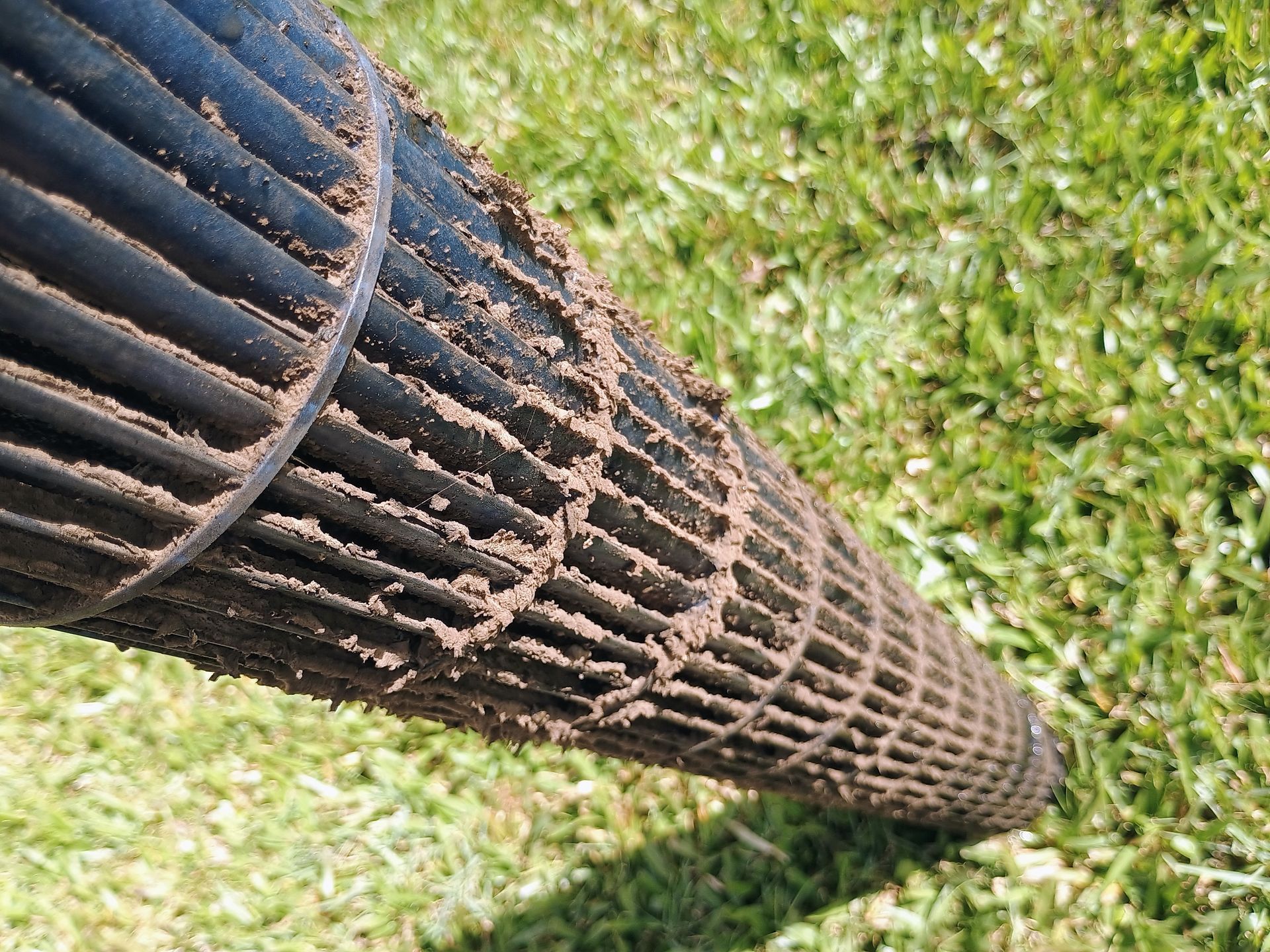 Dirty, cylindrical air filter covered in mud, resting on green grass.