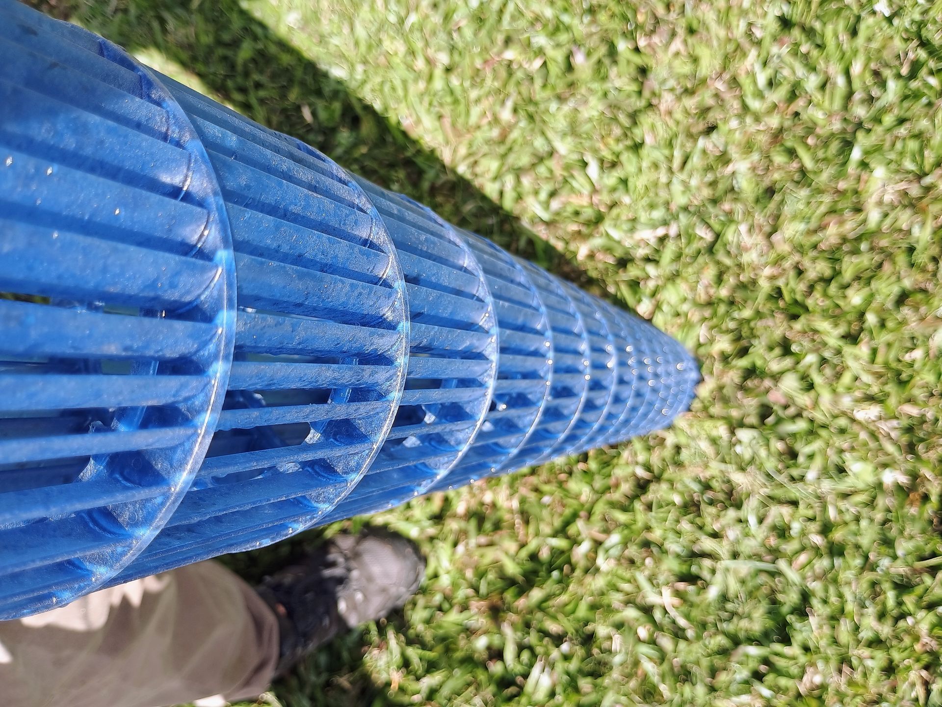 Blue cylindrical object with many circular sections on green grass.