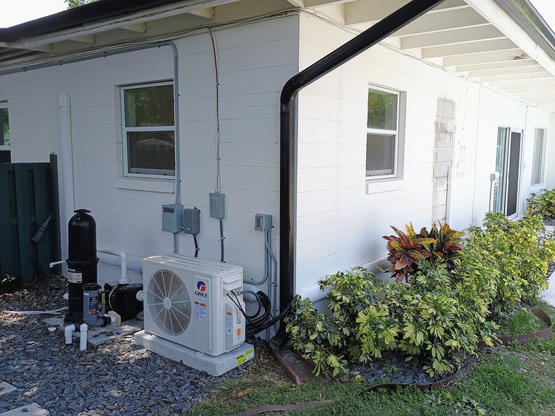 White building exterior with AC unit, electrical boxes, pool equipment, and landscaping.