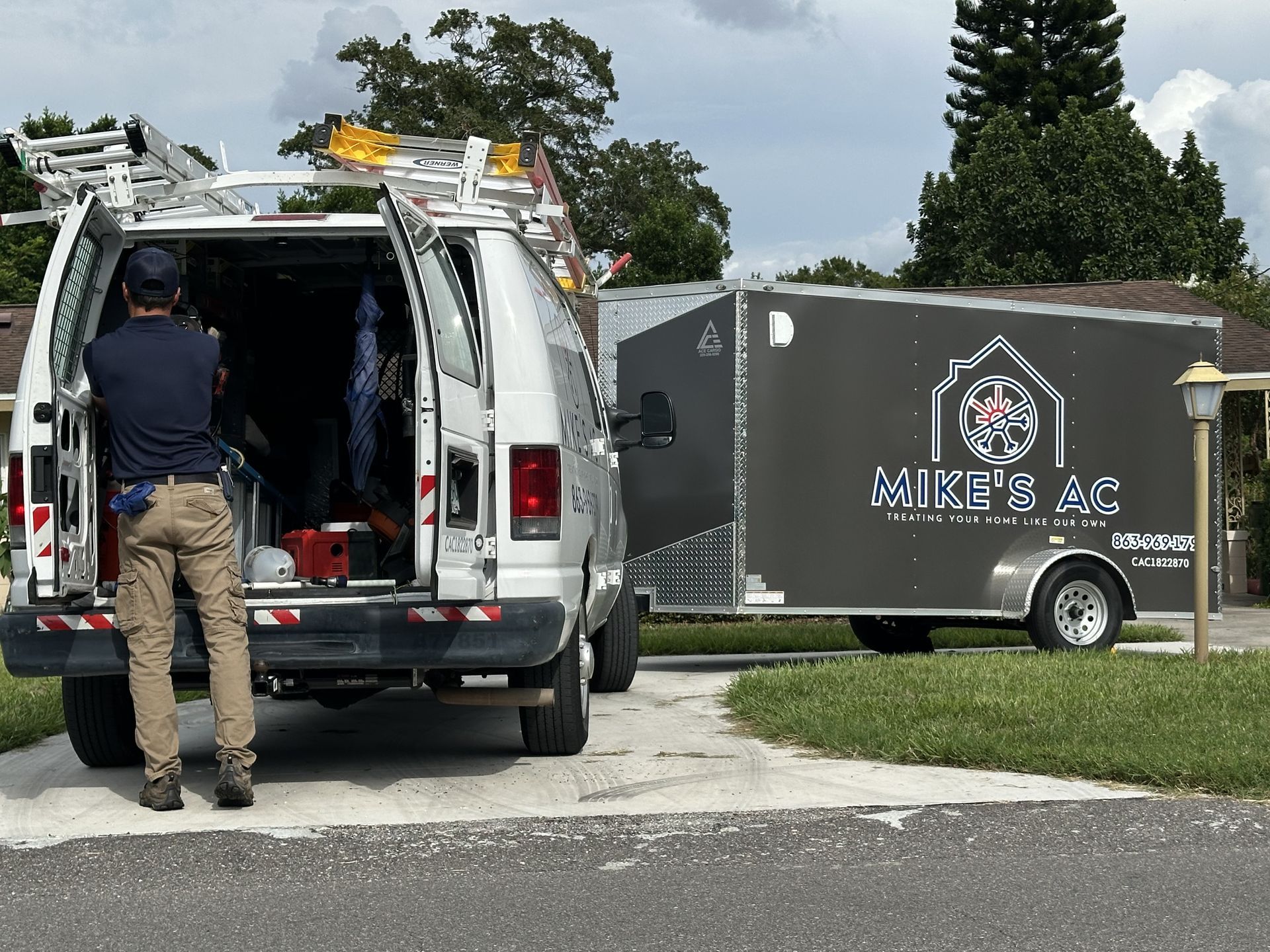 Man near van and trailer parked in a driveway. Trailer has 