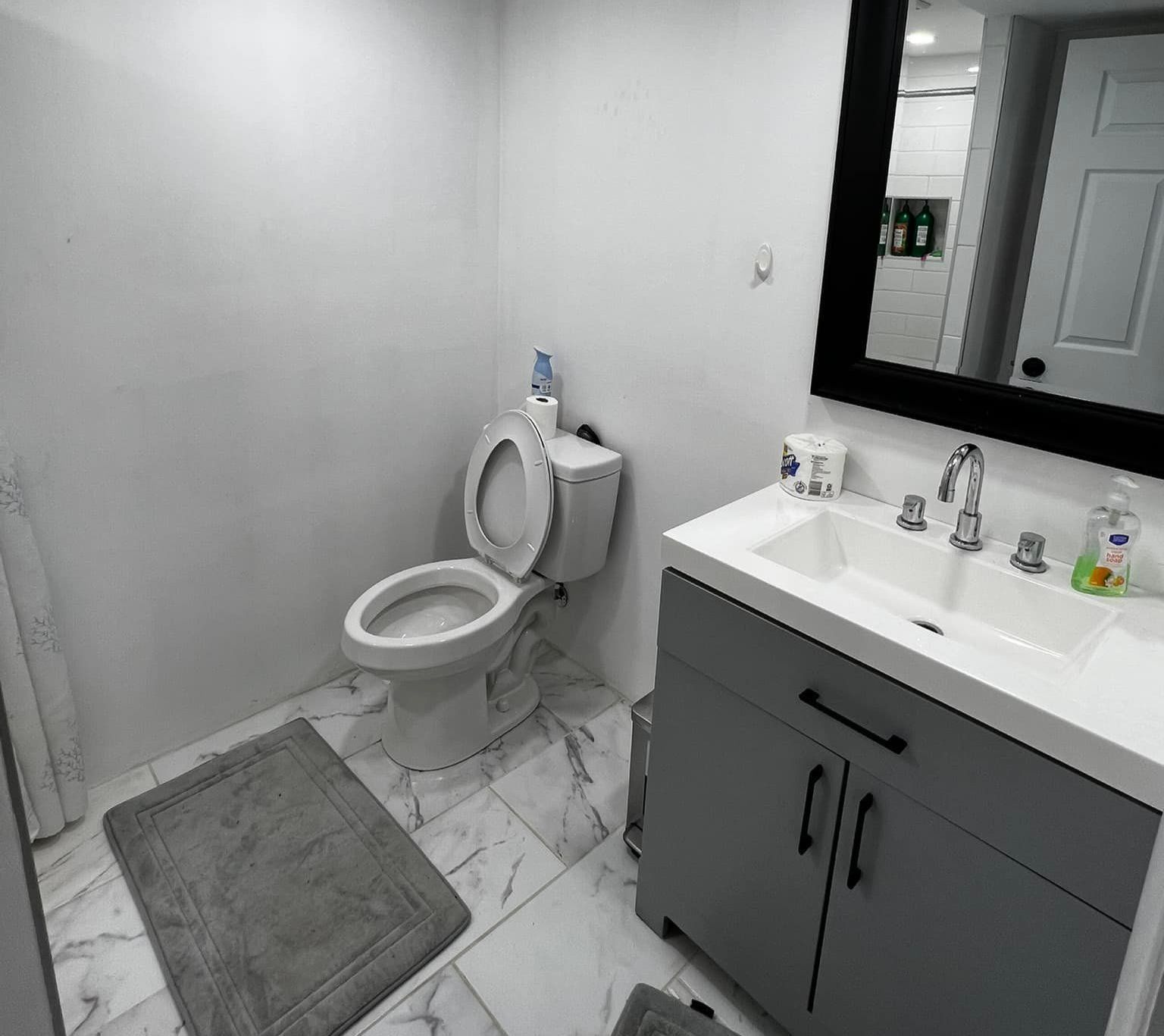 Bathroom with a toilet, vanity, and a framed mirror. White and gray tones throughout.