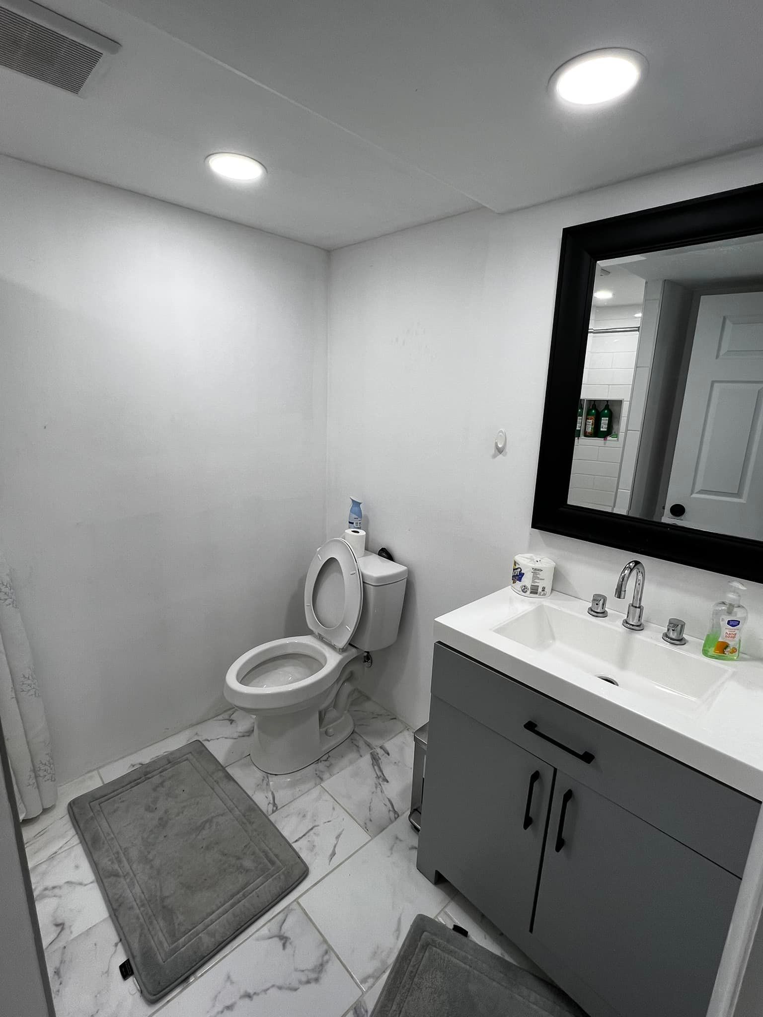 Bathroom with white walls, toilet, gray vanity, black-framed mirror, and gray rugs.