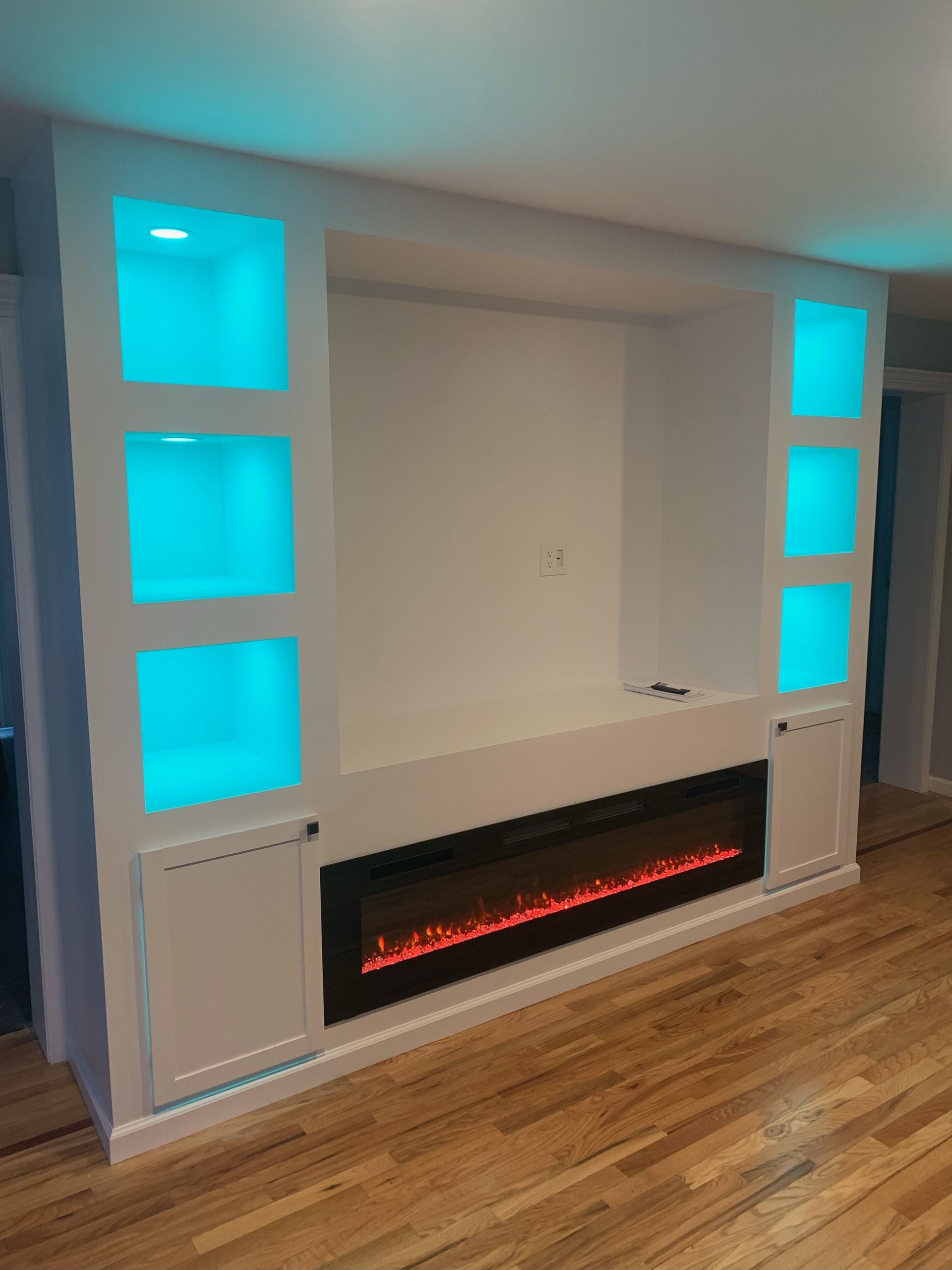 White entertainment center with electric fireplace and turquoise-lit shelves.