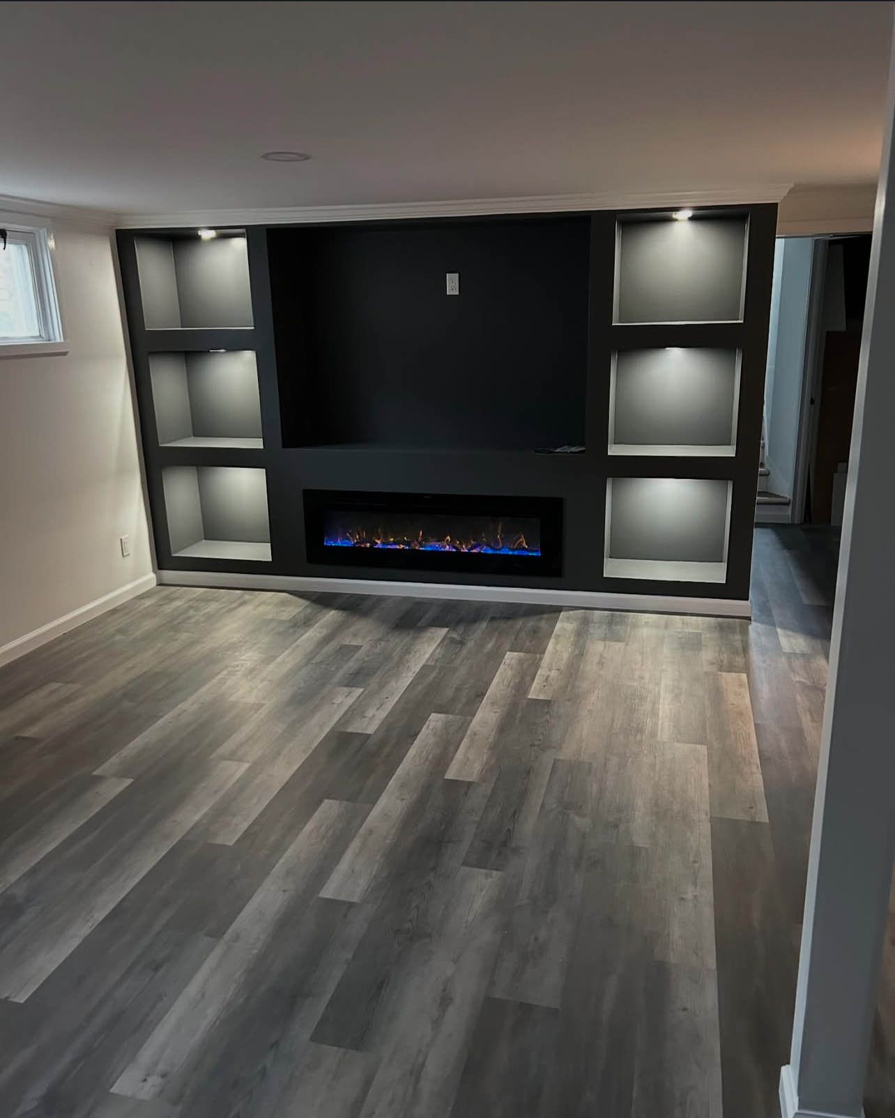 Gray-floored basement with a black built-in entertainment center. Fireplace, shelving, and recessed lighting.