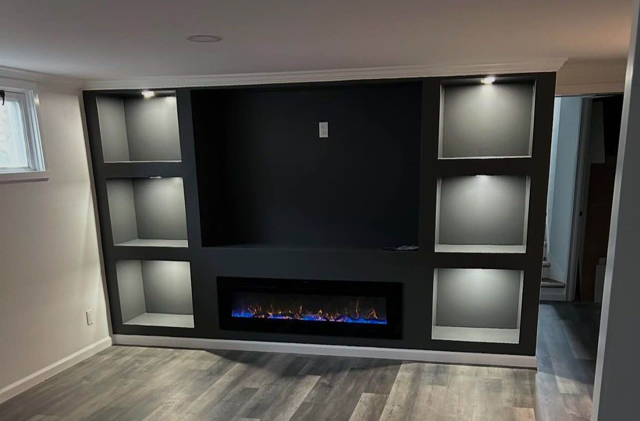 Built-in entertainment center with shelves, fireplace, and overhead lighting; painted dark gray; on gray wood-look floor.
