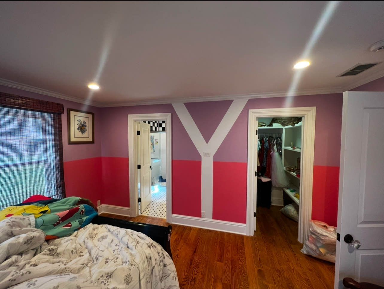 Bedroom with pink and purple walls, wooden floor, and two doorways. One leads to a closet, the other to a bathroom.