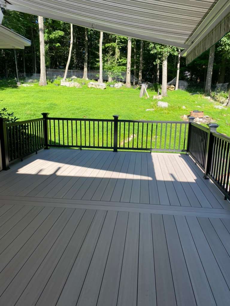 Deck with black railing, light-colored boards, and a grassy backyard with trees.