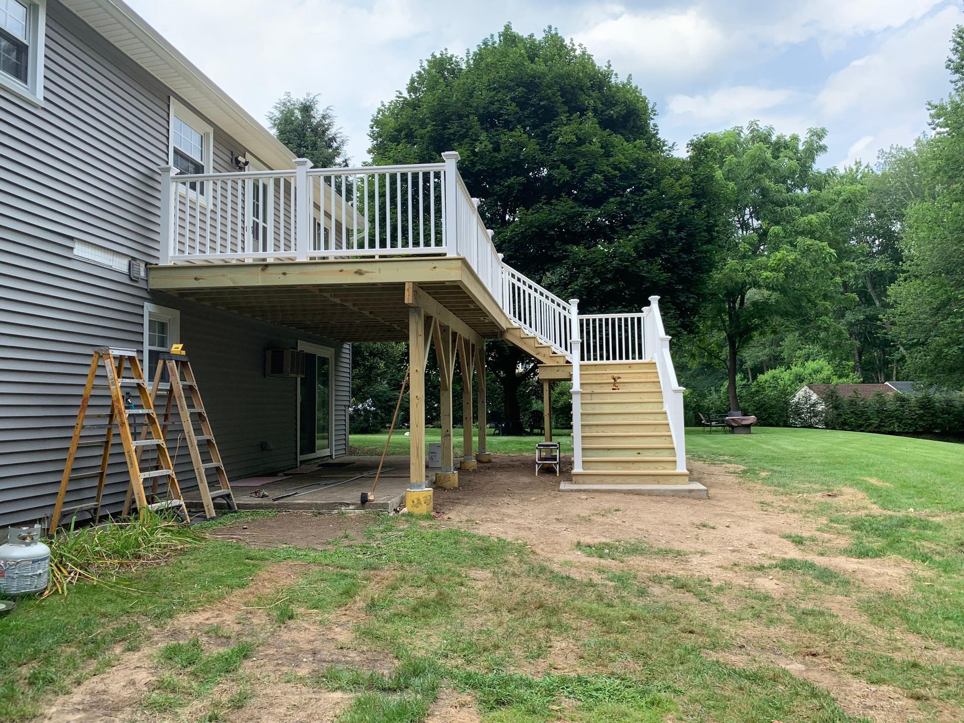 Wooden deck with white railing and stairs; next to a gray house, on a grassy yard.
