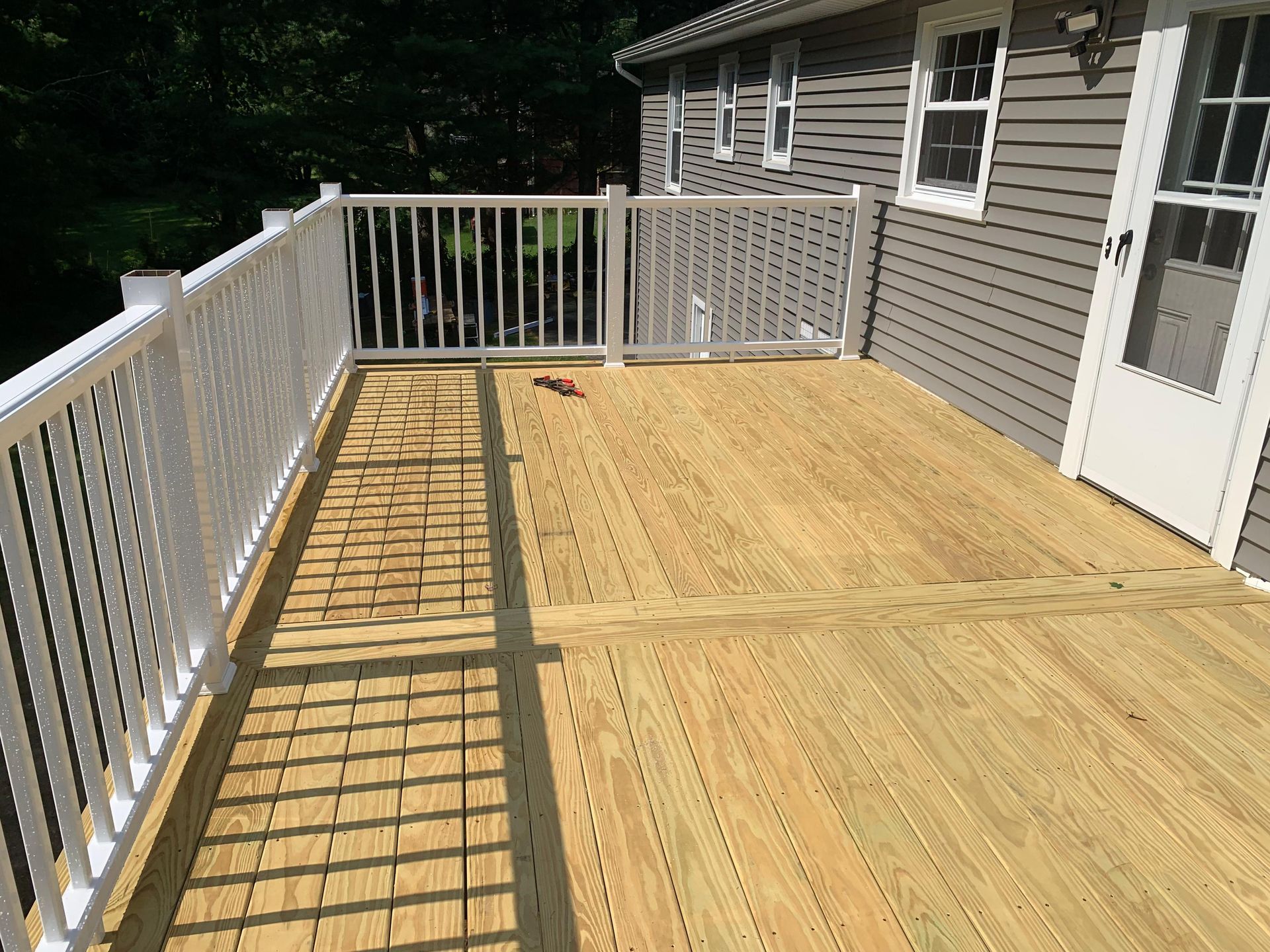 Wooden deck with white railing next to a house with gray siding.