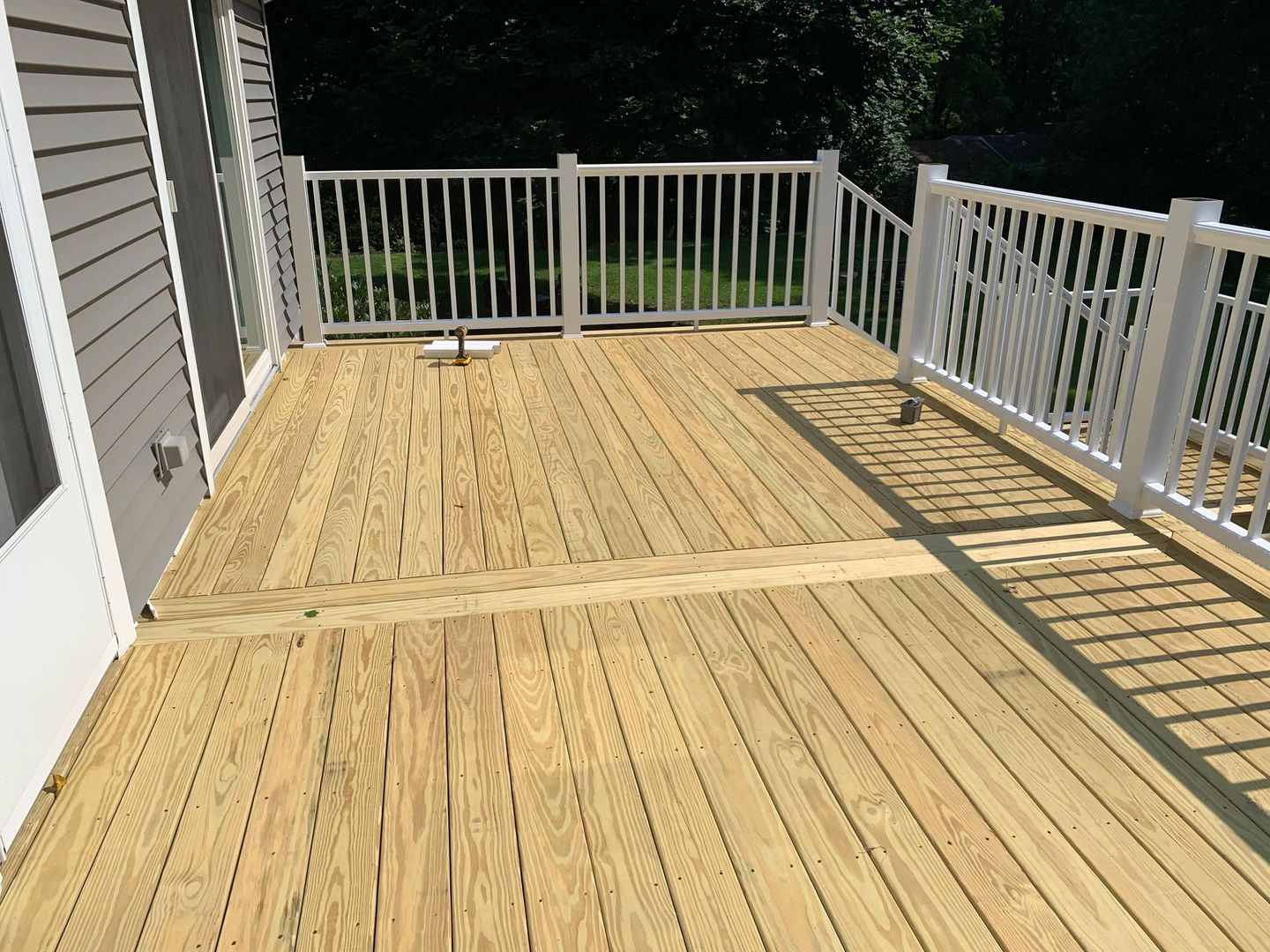 Wooden deck with white railing attached to a building with gray siding, sunlight.