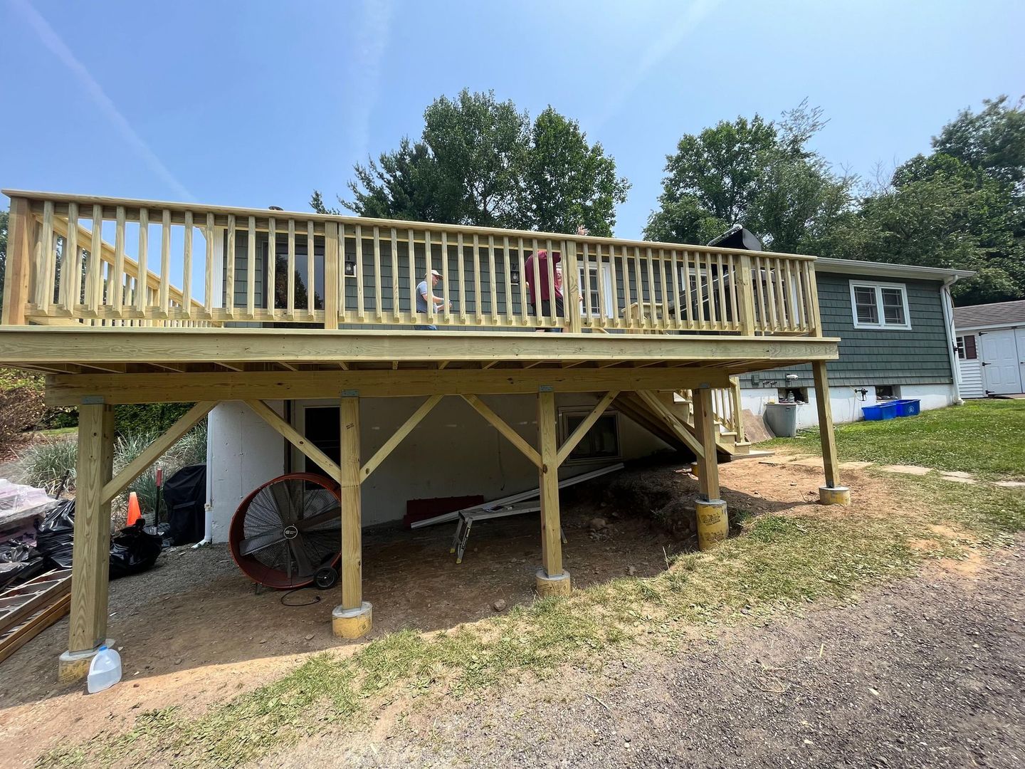Wooden deck raised above a gravel yard, supported by posts. A white structure is below.