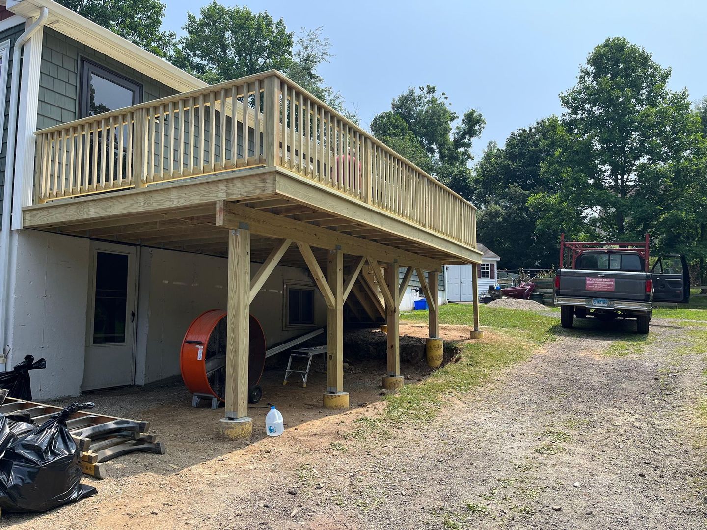 Wooden deck attached to a house with supporting posts. A truck is parked nearby.