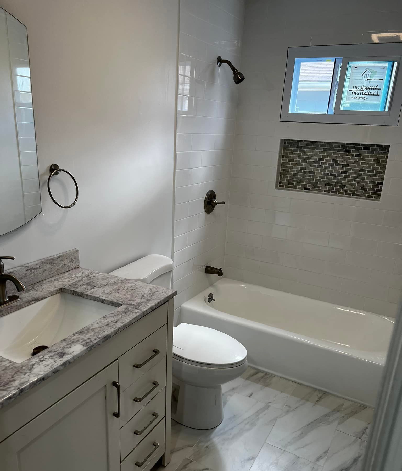 Modern white bathroom with vanity, toilet, and bathtub with mosaic niche.