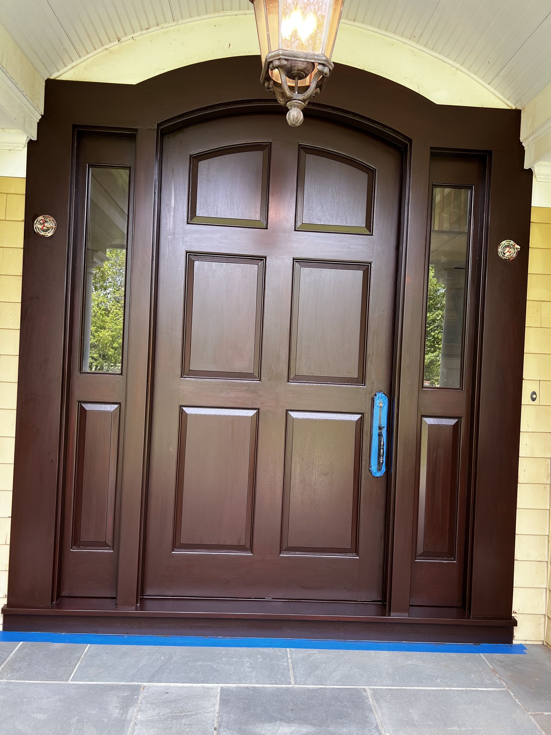 Brown wooden front door with sidelights, under a curved arch, and a hanging light fixture.