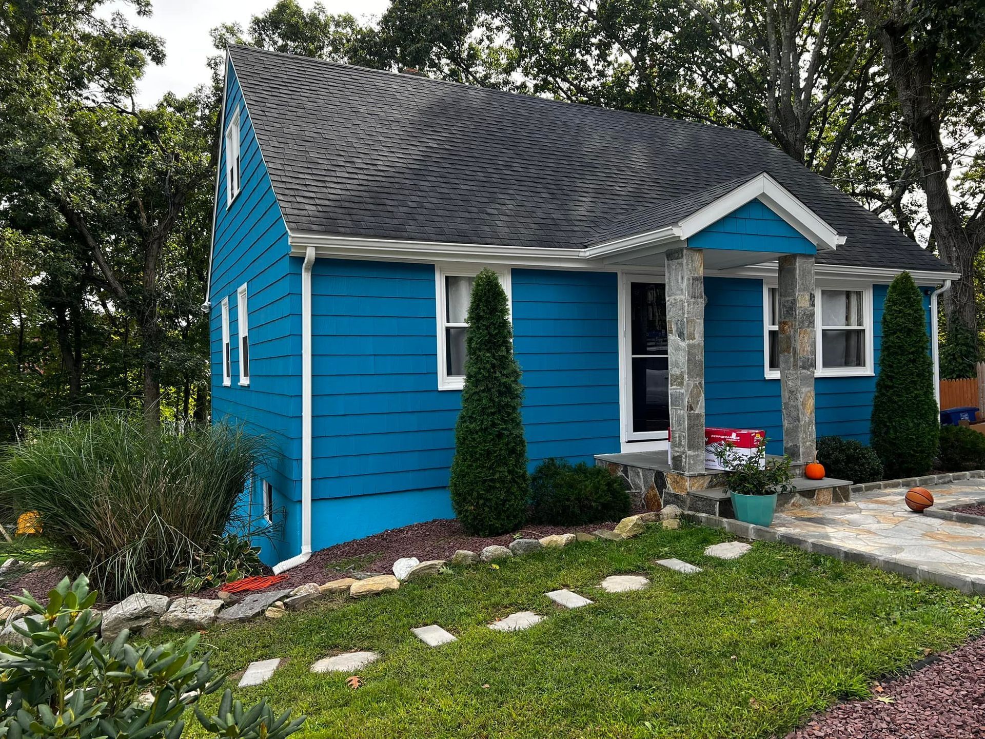 Blue house with white trim, gray roof, stone columns, and manicured lawn.