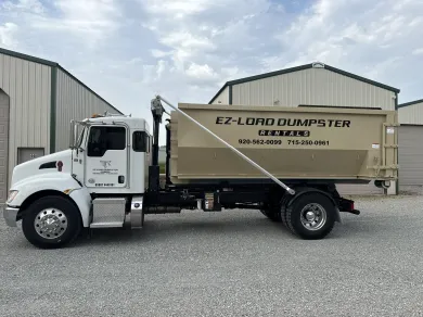 A row of dumpsters are parked in a gravel lot.