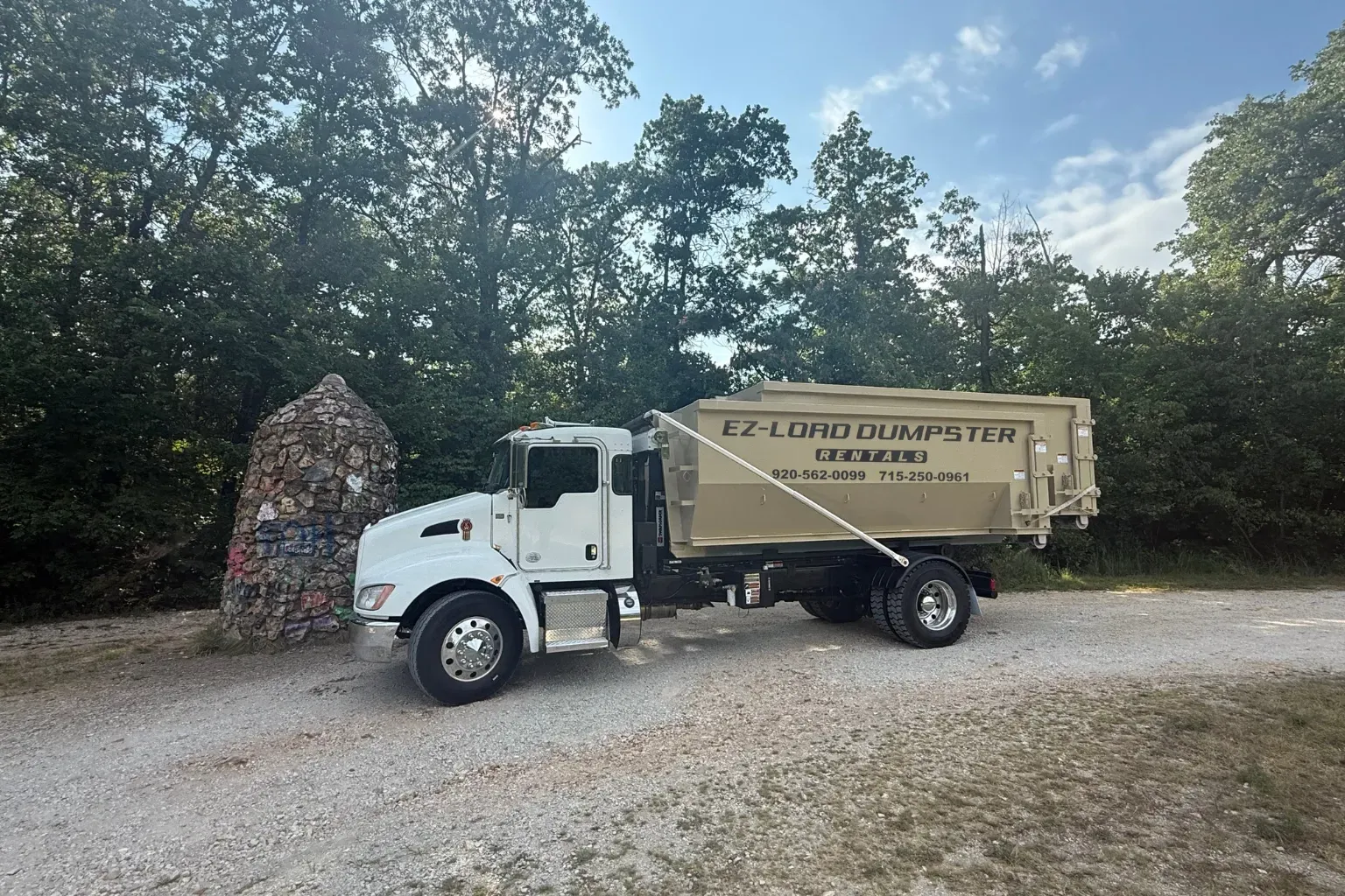A row of dumpsters are parked in a gravel lot.