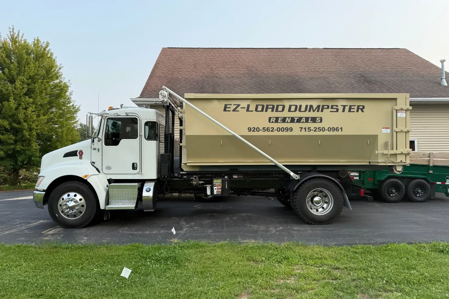 A dumpster is being pulled by a truck on a trailer.