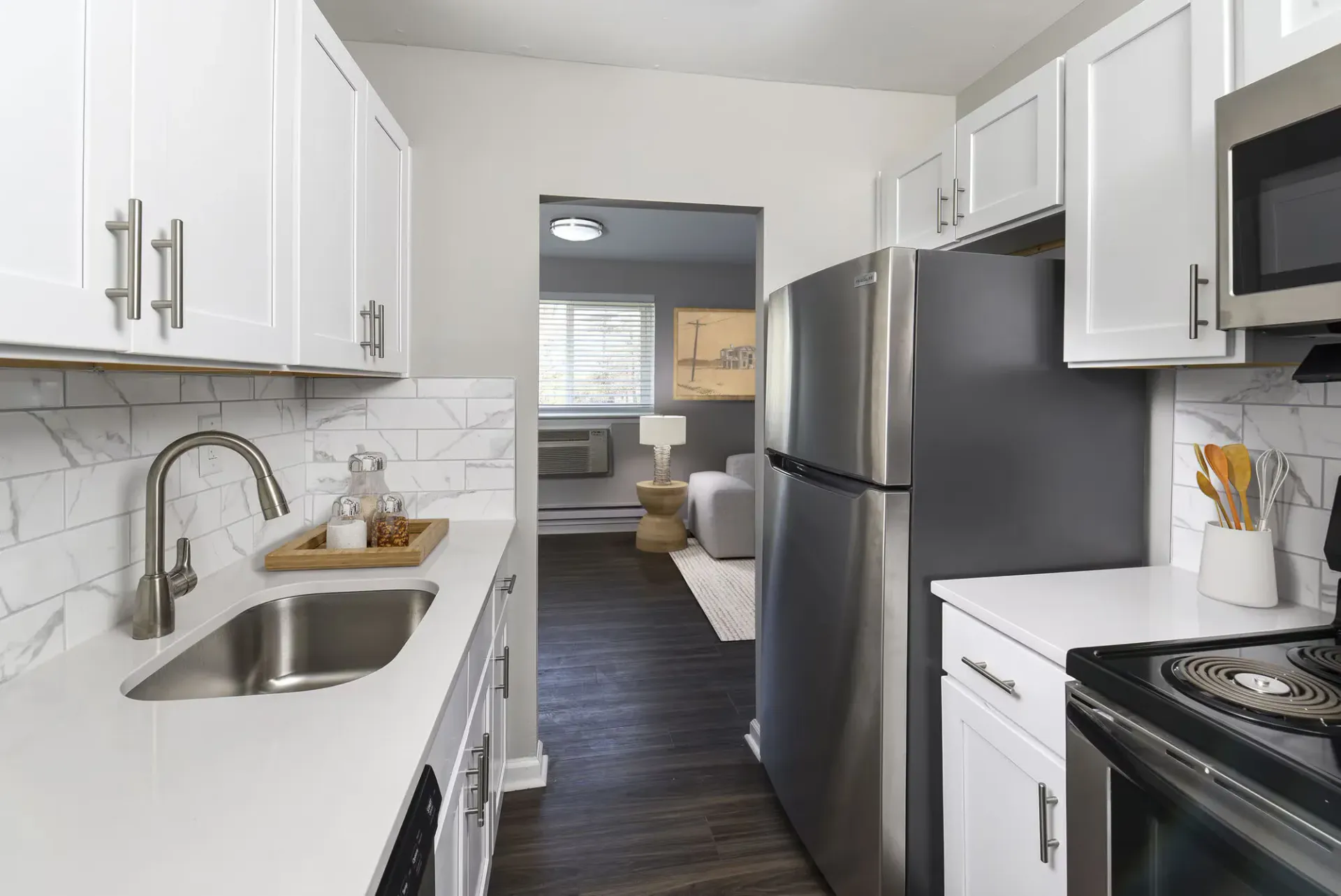 Modern apartment kitchen with white cabinets, marble backsplash, stainless steel fridge, and sink at The Addison, offers townhomes for rent in North Wales, PA.
