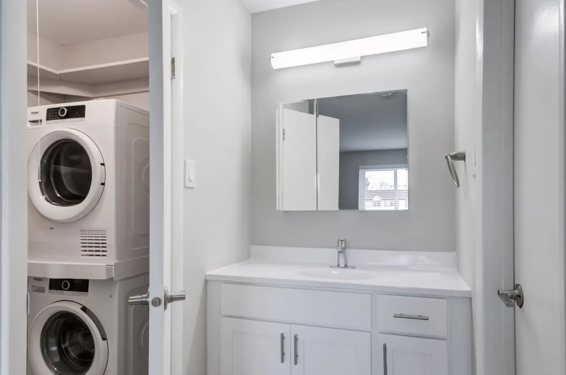 Bathroom vanity with sink and mirror, adjacent laundry closet with stacked washer/dryer at The Addison, offers townhomes in North Wales, PA.