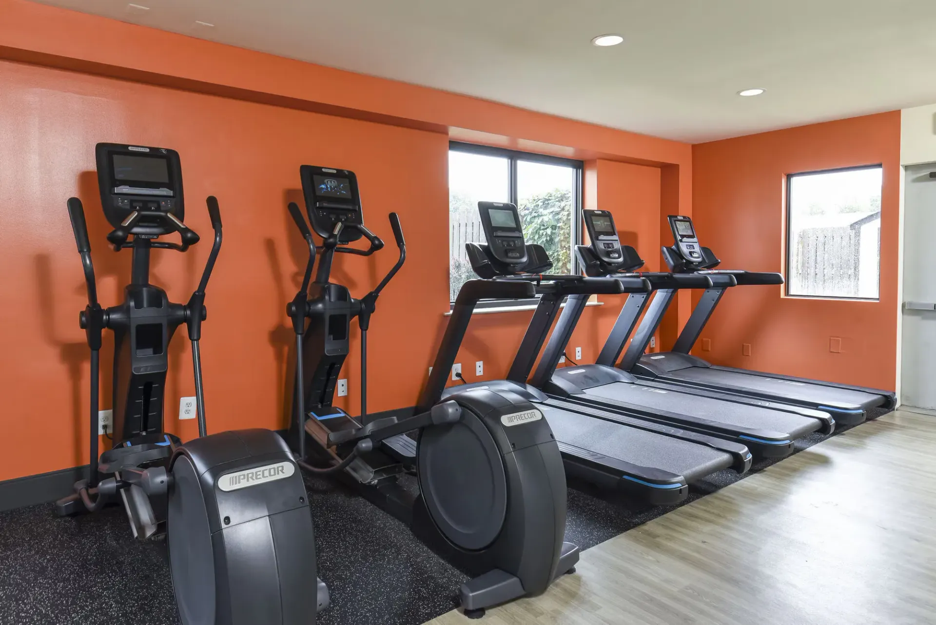 Cardio machines (treadmills and ellipticals) in a bright orange-walled community gym at The Addison, offers apartments in North Wales, PA.